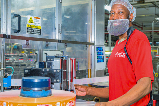 Man in production facility wearing red Coca-Cola polo shirt