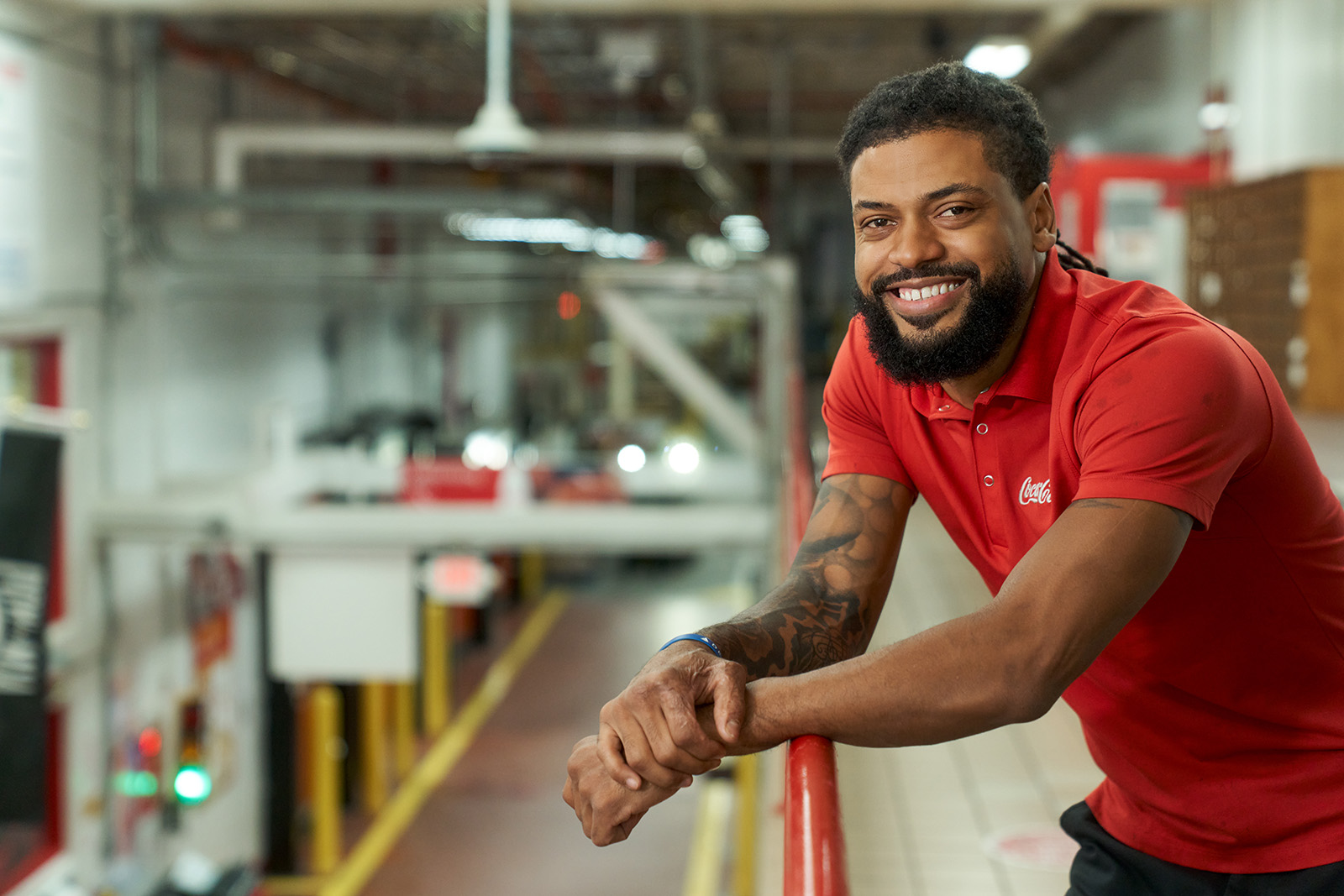 Man in Coca-Cola polo shirt smiling leaning on a railing at manufacturing facility